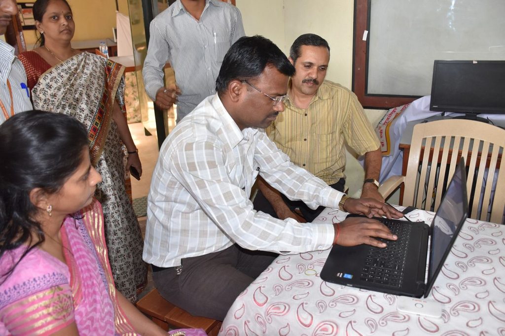 Adults follow a computer training session seated at desks in a bright classroom.